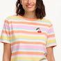 A woman modeling a multicolored striped t-shirt with a small embroidered cherry on the chest, paired with a blue denim skirt.
