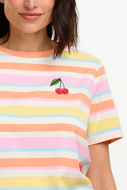 A woman modeling a multicolored striped t-shirt with a small embroidered cherry on the chest, paired with a blue denim skirt.
