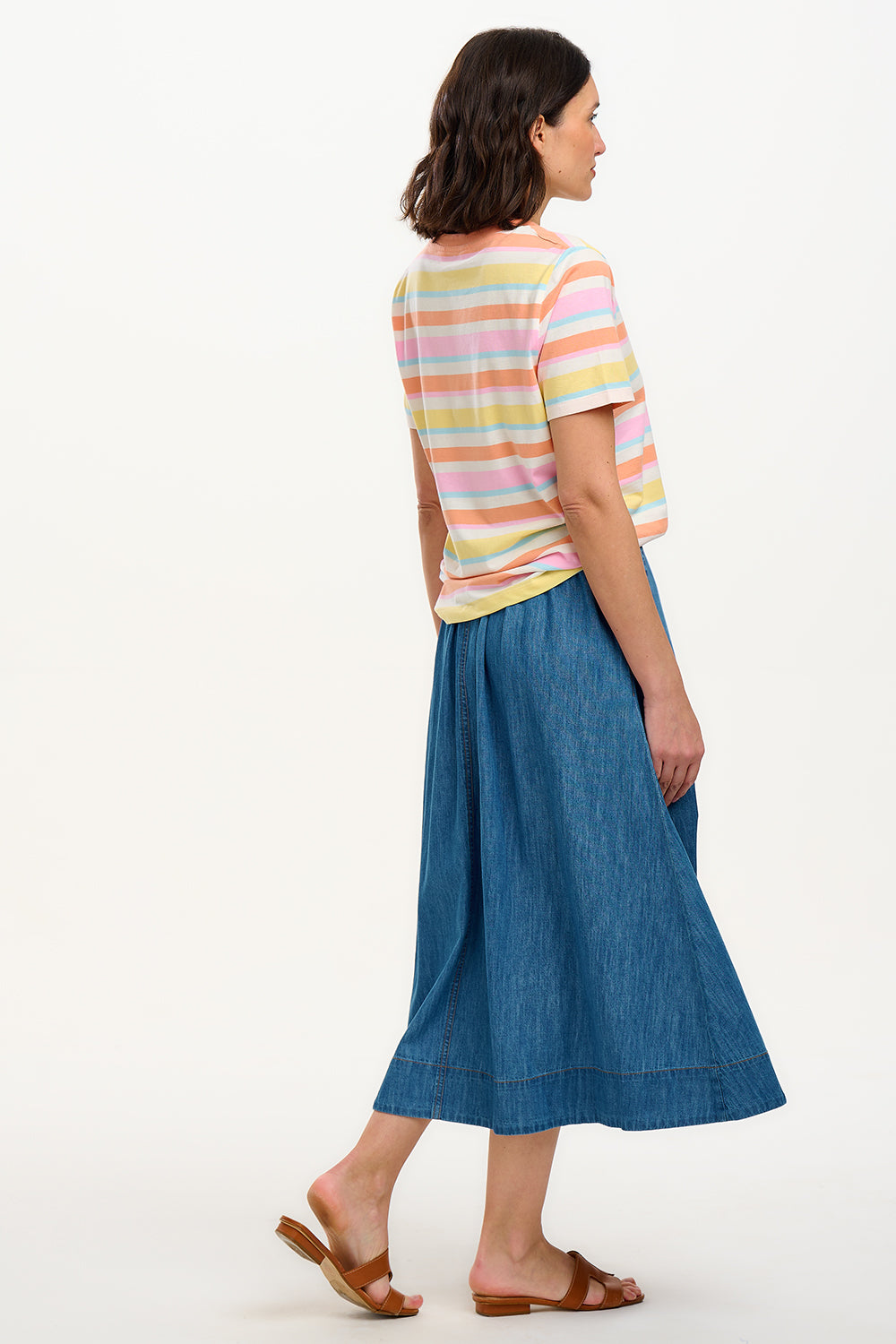 A woman modeling a multicolored striped t-shirt with a small embroidered cherry on the chest, paired with a blue denim skirt.