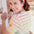 A woman smiling and wearing a multicolored striped t-shirt with a flower face detail on the chest.