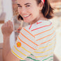 A woman smiling and wearing a multicolored striped t-shirt with a flower face detail on the chest.