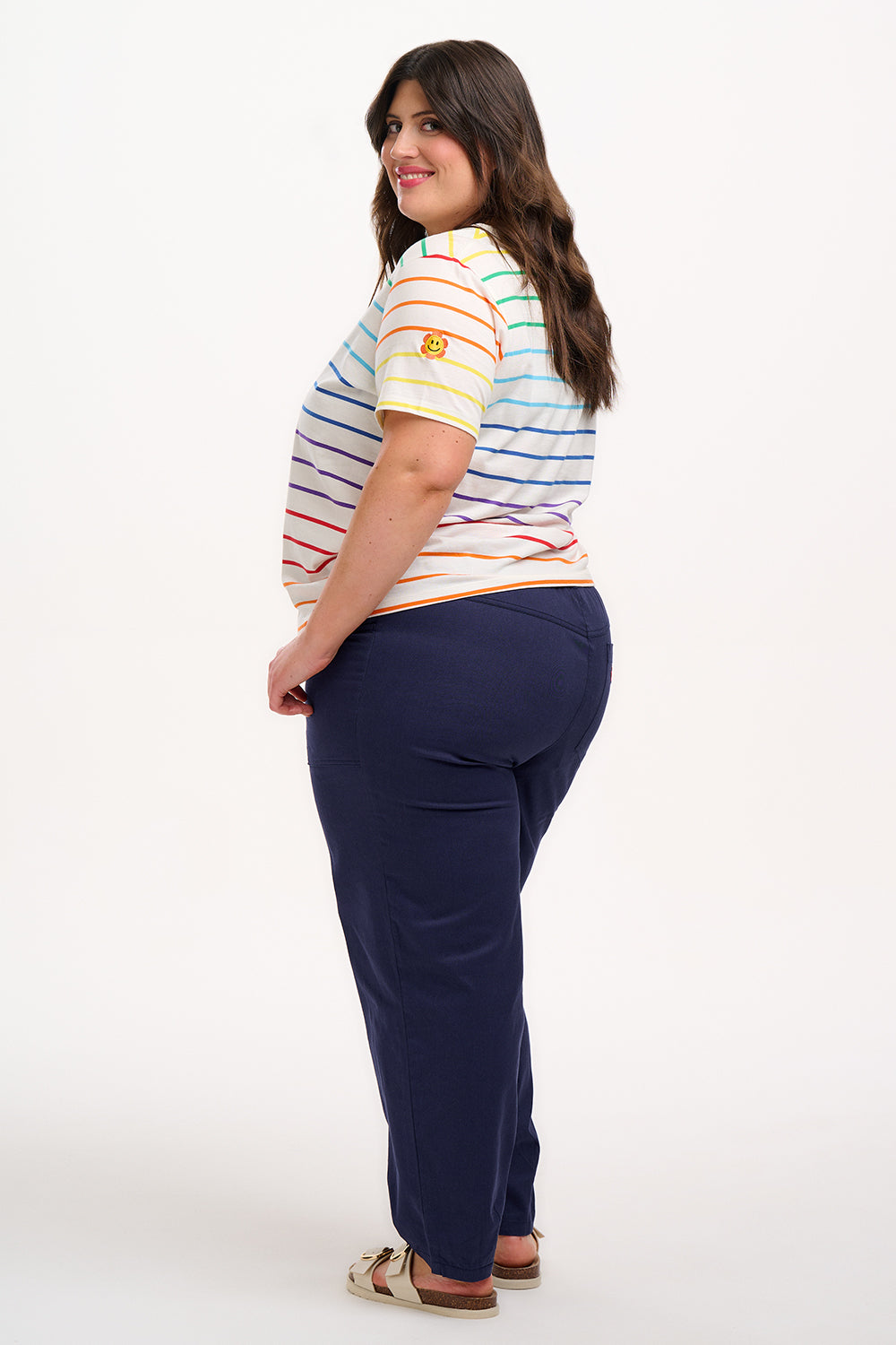 A woman smiling and posing in a multicolored striped t-shirt with a crew neck, featuring a small logo on the upper left chest.