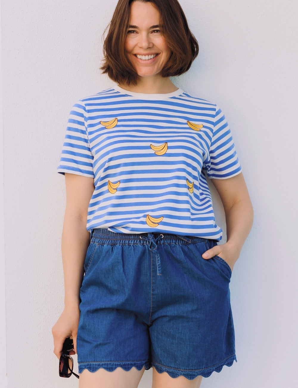 Woman wearing a blue and white striped shirt with banana prints and blue shorts against a plain background