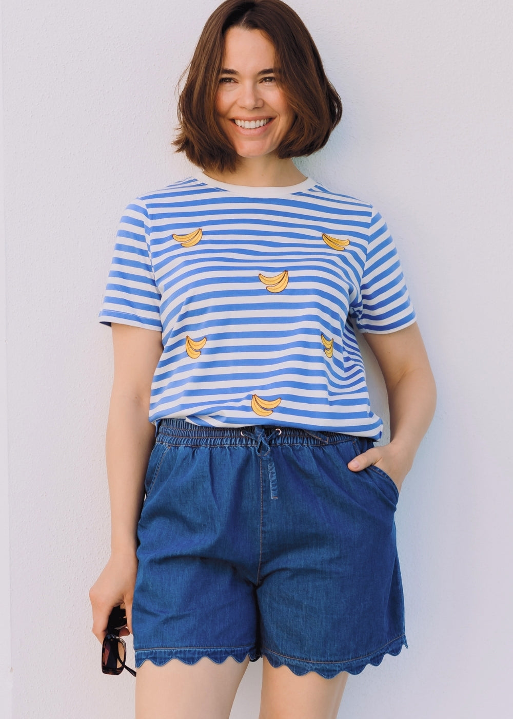 Woman wearing a blue and white striped shirt with banana prints and blue shorts against a plain background