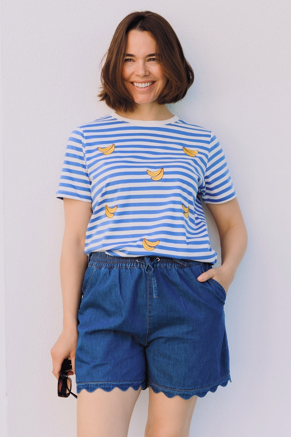 Woman wearing a blue and white striped shirt with banana prints and blue shorts against a plain background