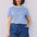 Woman wearing a blue and white striped shirt with banana prints and blue shorts against a plain background