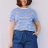 Woman wearing a blue and white striped shirt with banana prints and blue shorts against a plain background