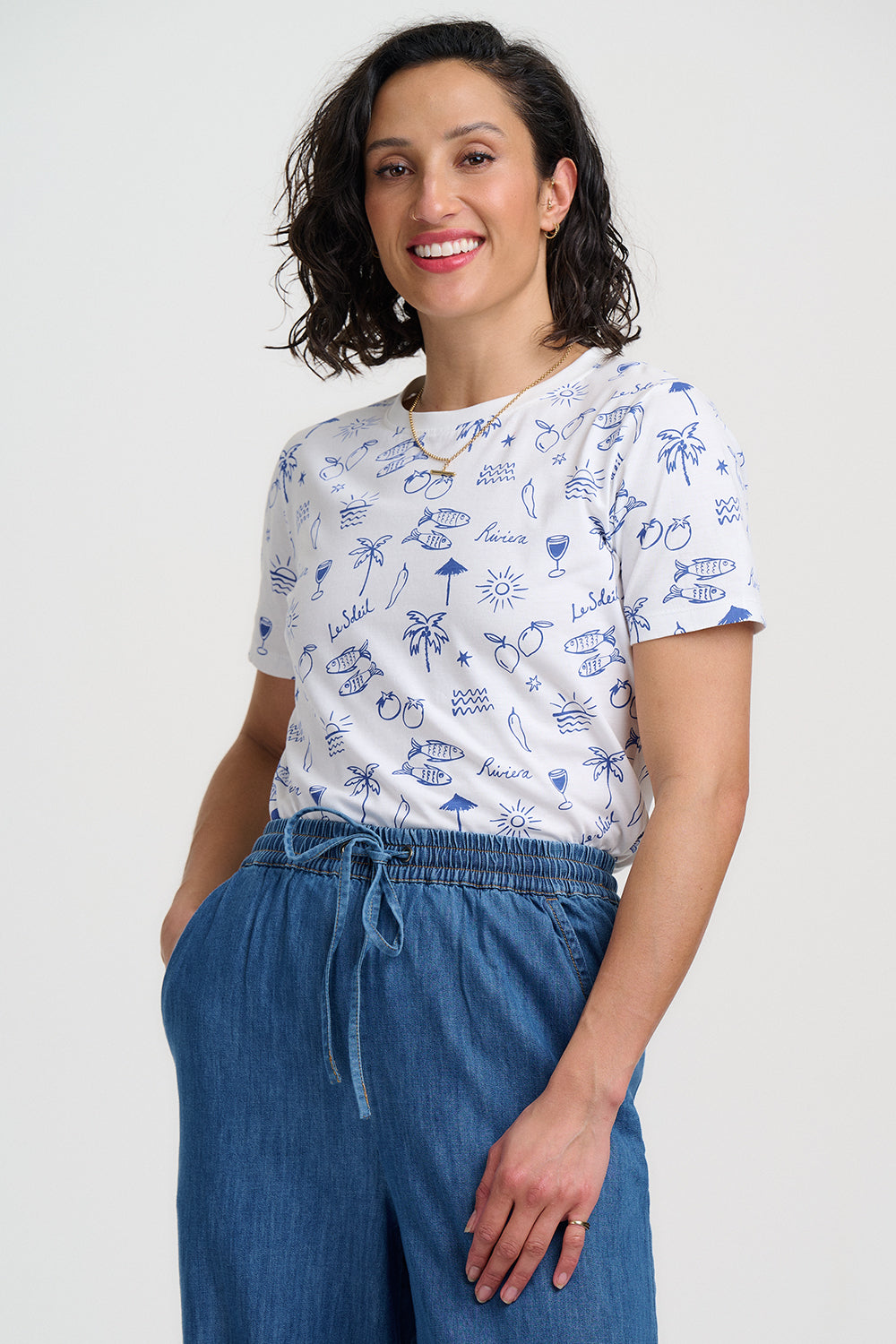Woman wearing a white t-shirt with blue patterns and blue pants on a white background