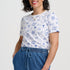 Woman wearing a white t-shirt with blue patterns and blue pants on a white background