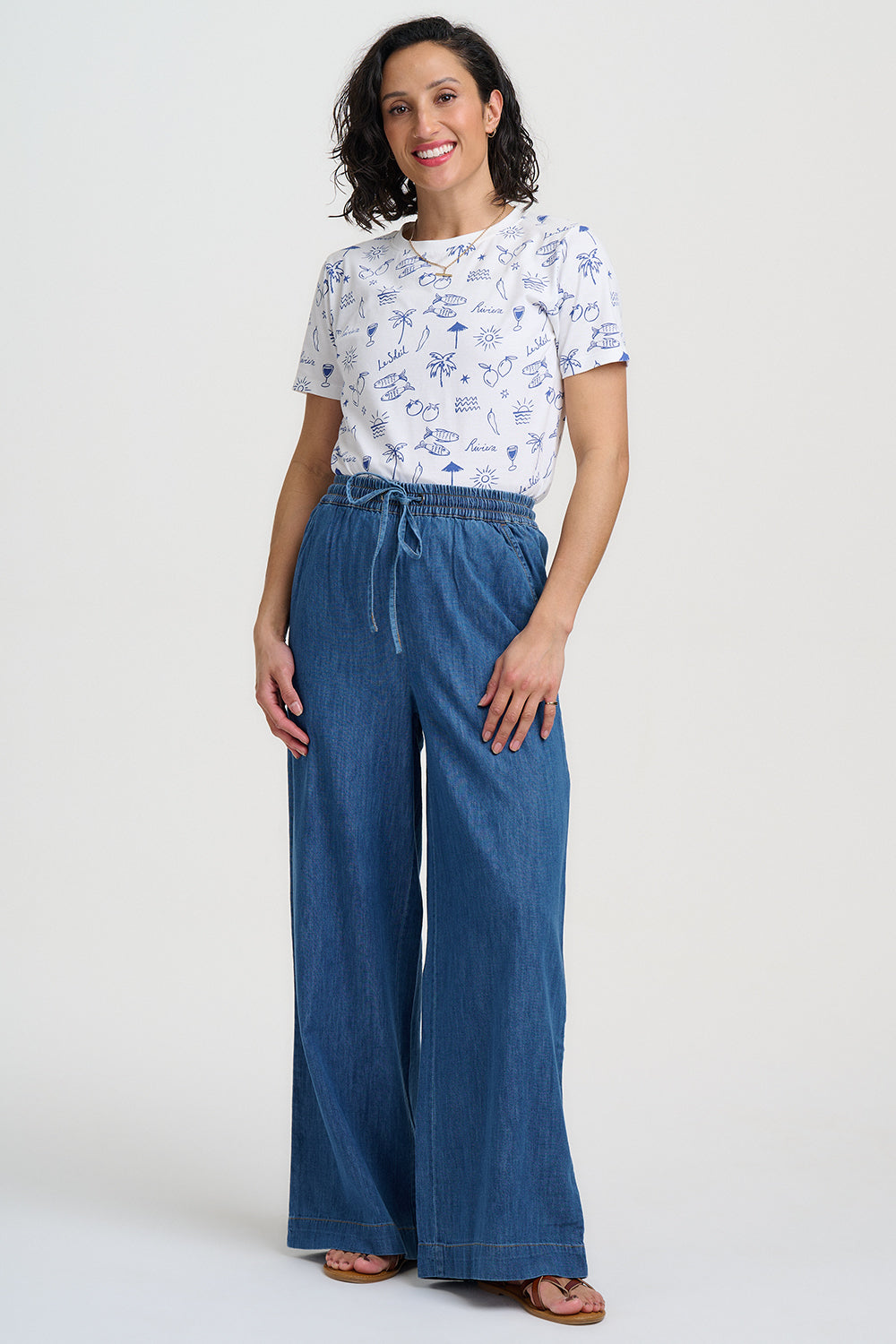 Woman wearing a white t-shirt with blue patterns and blue wide-leg pants on a white background