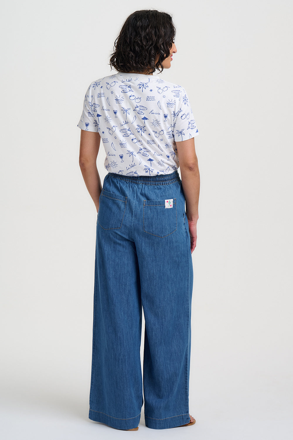 Person wearing a white patterned shirt and blue wide-leg pants on a white background