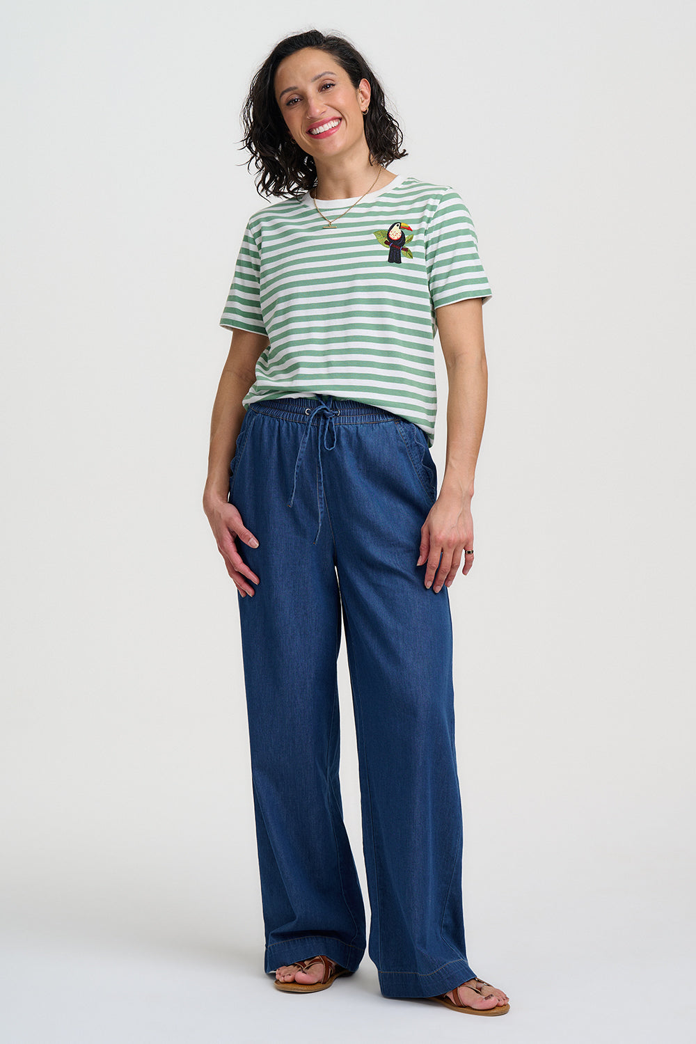 Woman wearing a green and white striped shirt and blue pants on a white background