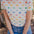 A person wearing an off-white t-shirt with a colorful dinosaur print, paired with blue jeans.