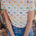 A person wearing an off-white t-shirt with a colorful dinosaur print, paired with blue jeans.