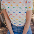 A person wearing an off-white t-shirt with a colorful dinosaur print, paired with blue jeans.