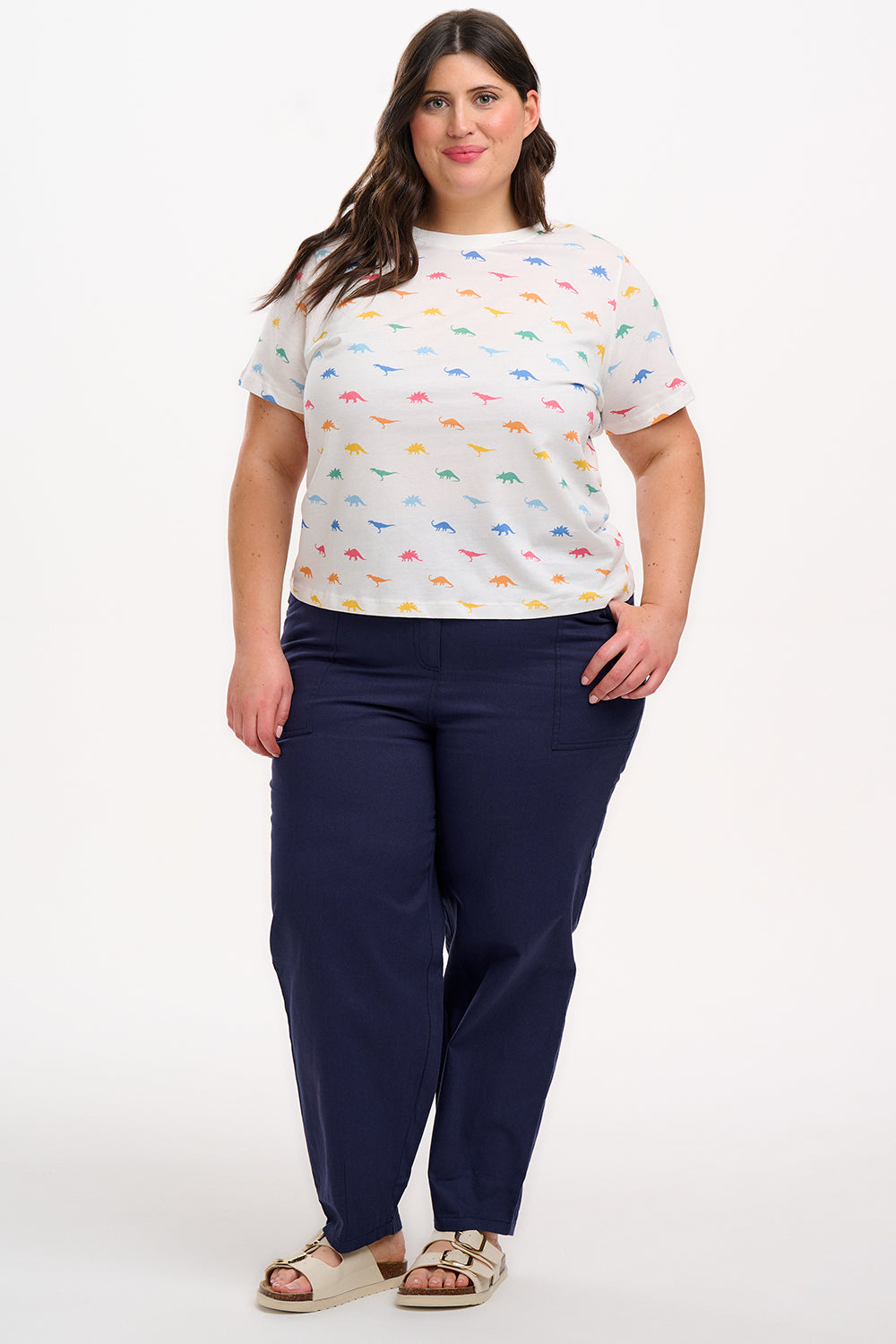 A woman wearing an off-white t-shirt with a colorful dinosaur print, paired with blue jeans.
