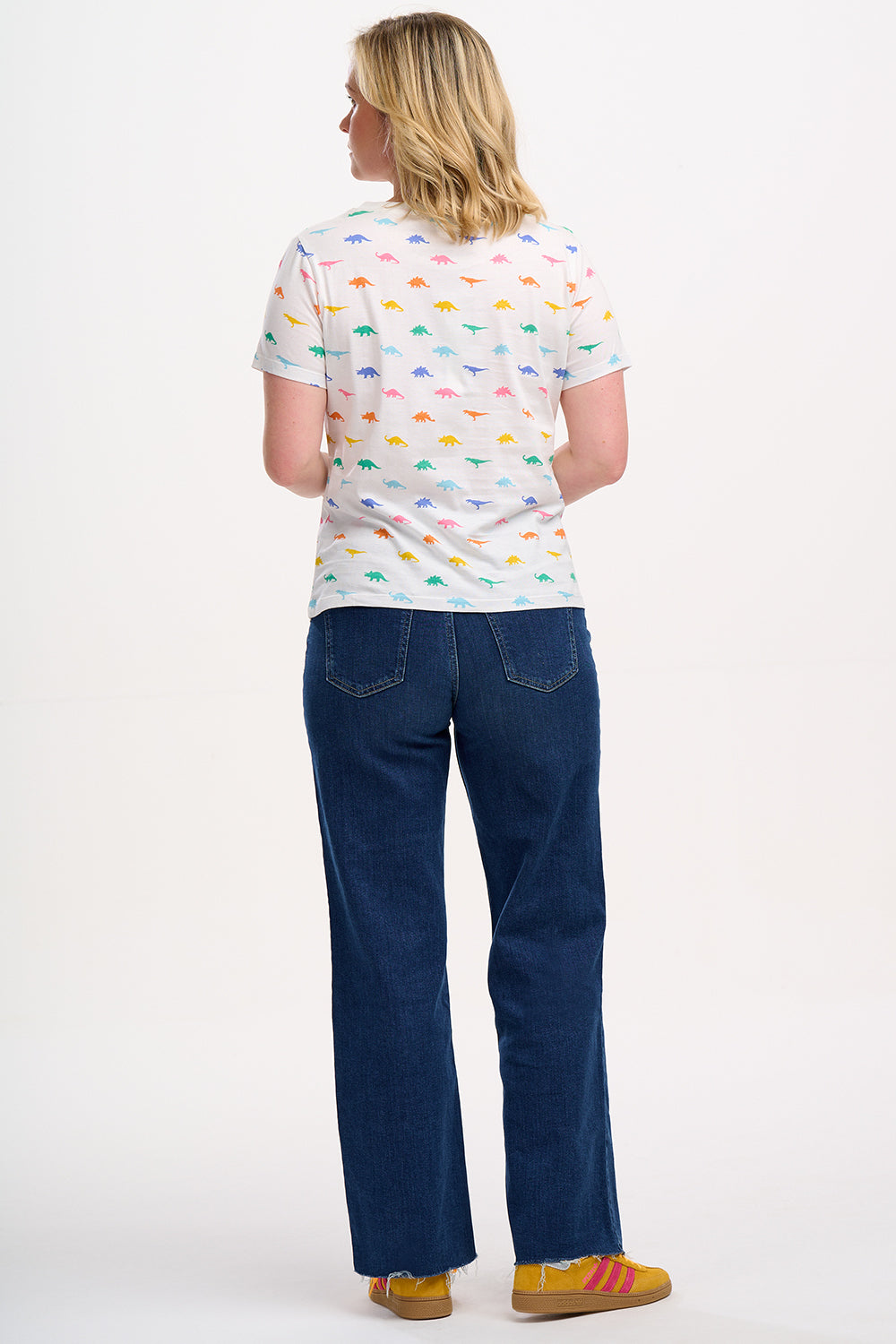 A woman wearing an off-white t-shirt with a colorful dinosaur print, paired with blue jeans.