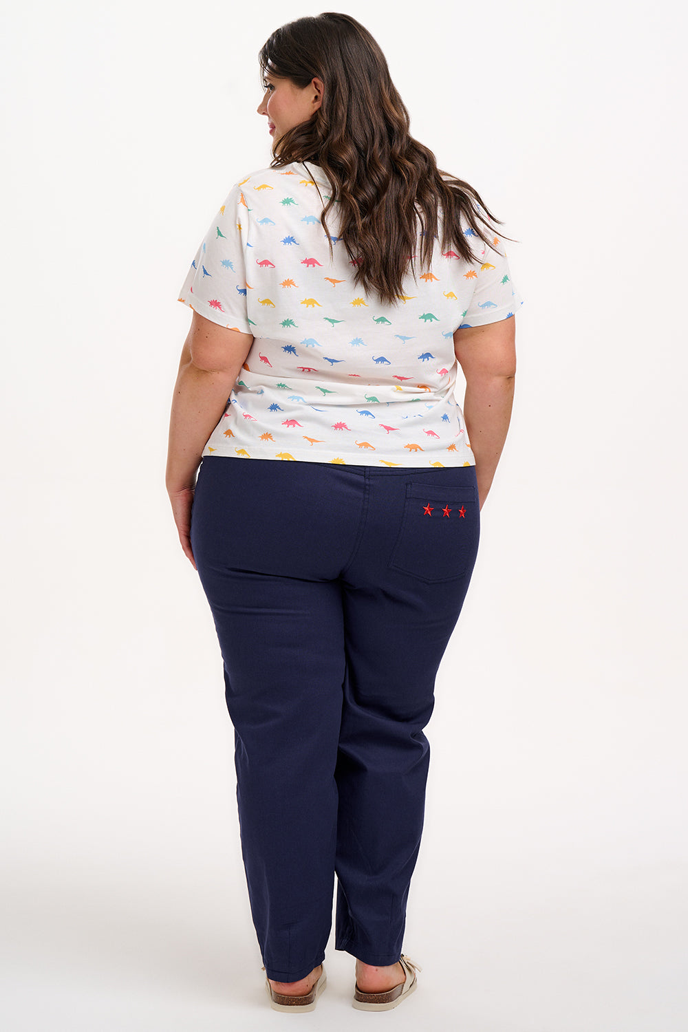 A woman wearing an off-white t-shirt with a colorful dinosaur print, paired with blue jeans.