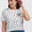 Woman wearing a white polka dot t-shirt with a colorful bird design on a plain background