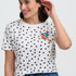 Woman wearing a white polka dot t-shirt with a colorful bird design on a plain background