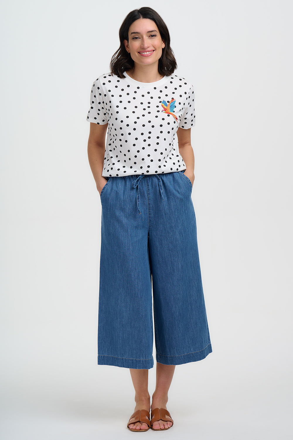 Woman wearing a polka dot shirt and blue wide-leg pants on a white background