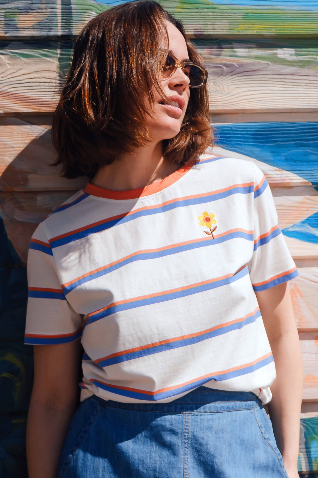 Person wearing a striped shirt with a flower design, standing against a colorful wooden wall.