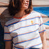 Person wearing a striped shirt with a flower design, standing against a colorful wooden wall.