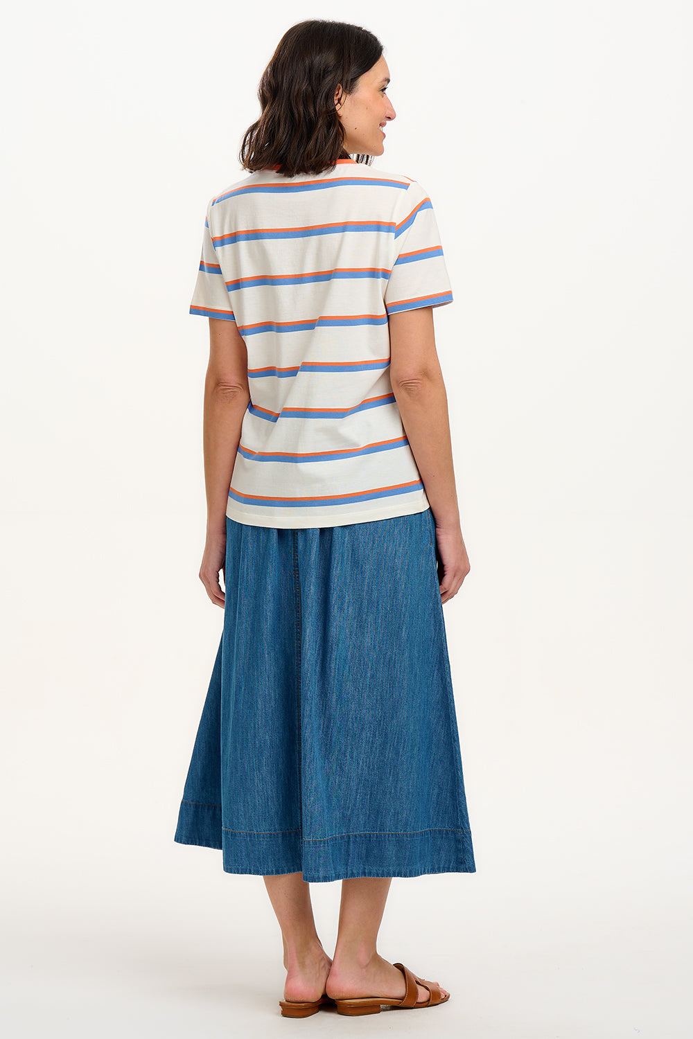 A woman smiling and wearing an off-white t-shirt with blue and orange stripes and a retro style embroidered flower on the chest, paired with a blue skirt.