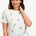 A woman smiling and wearing an off-white t-shirt with a pattern of small, colorful floral sprigs.