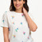 A woman smiling and wearing an off-white t-shirt with a pattern of small, colorful floral sprigs.