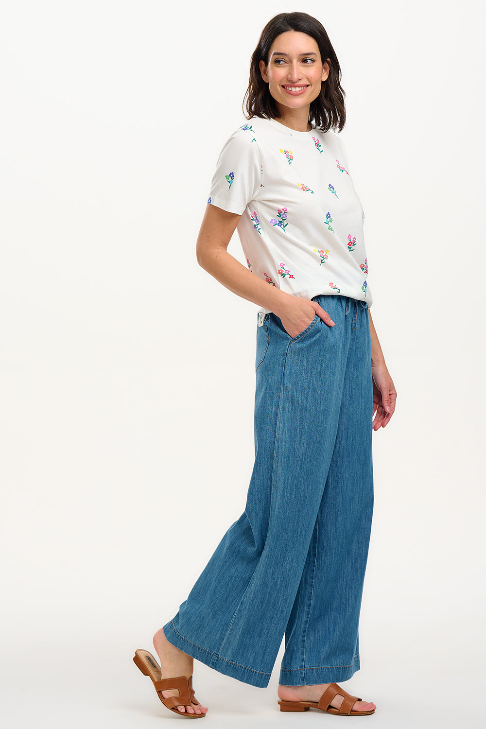 A woman smiling and wearing an off-white t-shirt with a pattern of small, colorful floral sprigs.