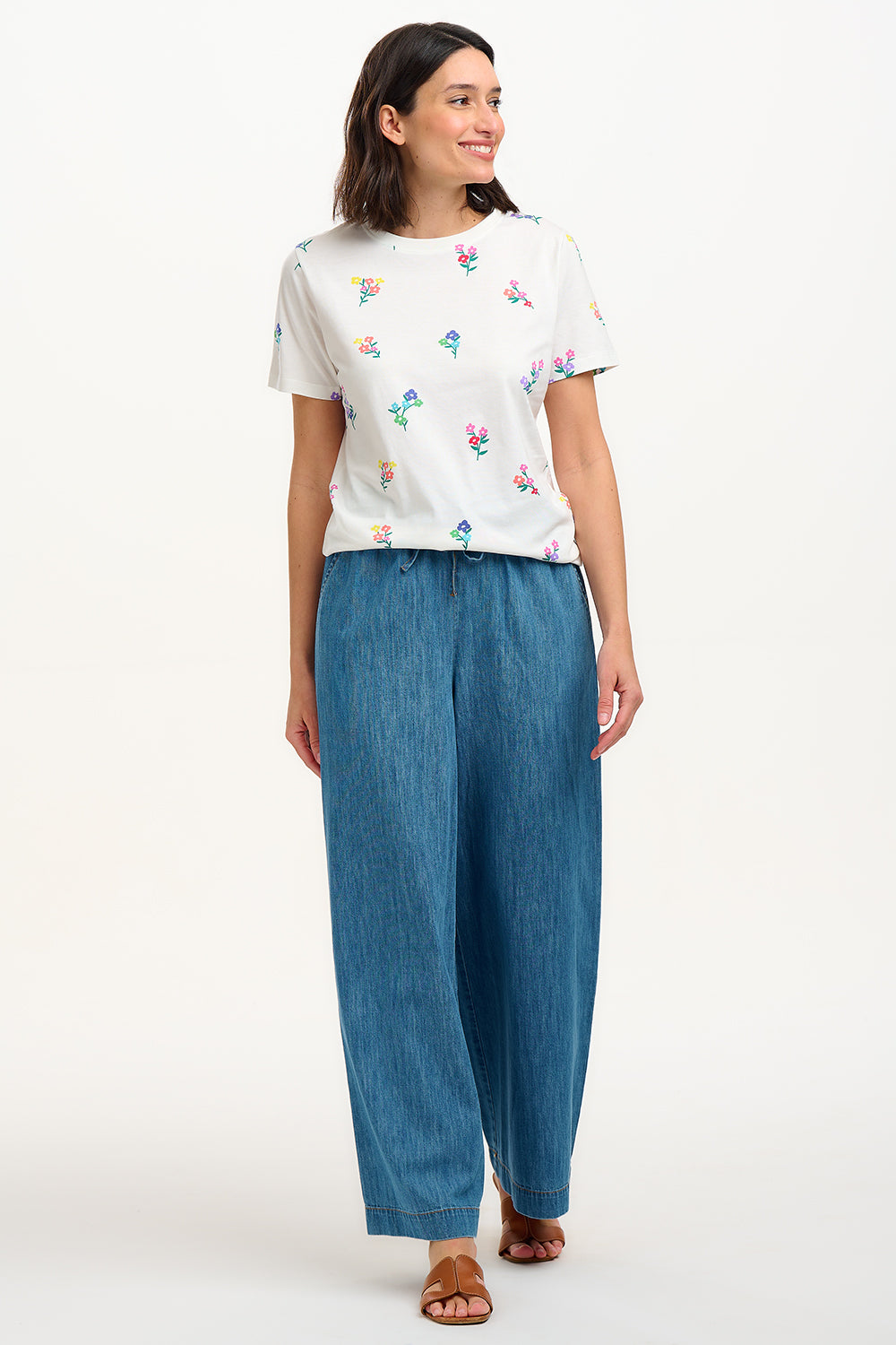 A woman smiling and wearing an off-white t-shirt with a pattern of small, colorful floral sprigs.