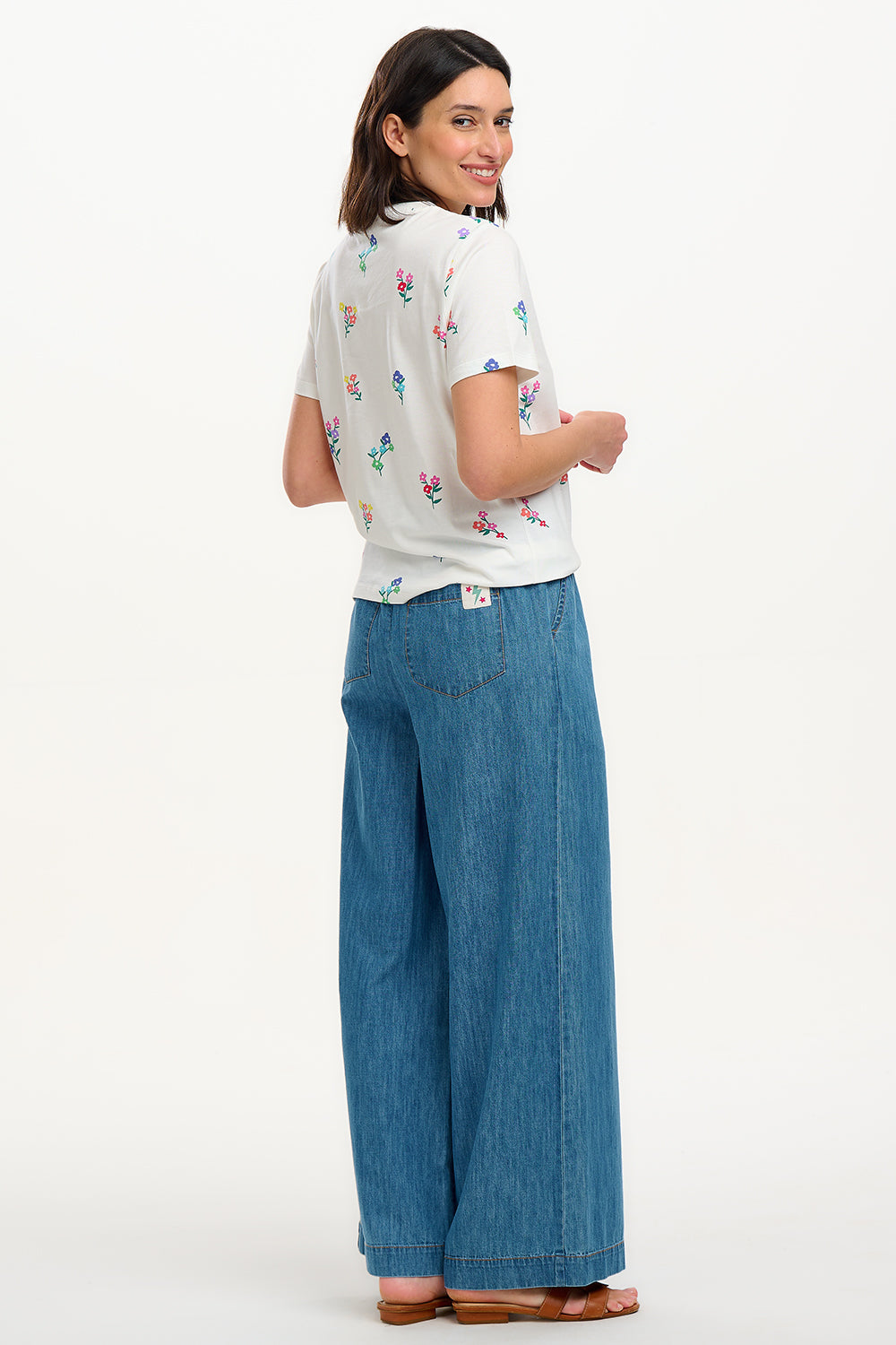A woman smiling and wearing an off-white t-shirt with a pattern of small, colorful floral sprigs.