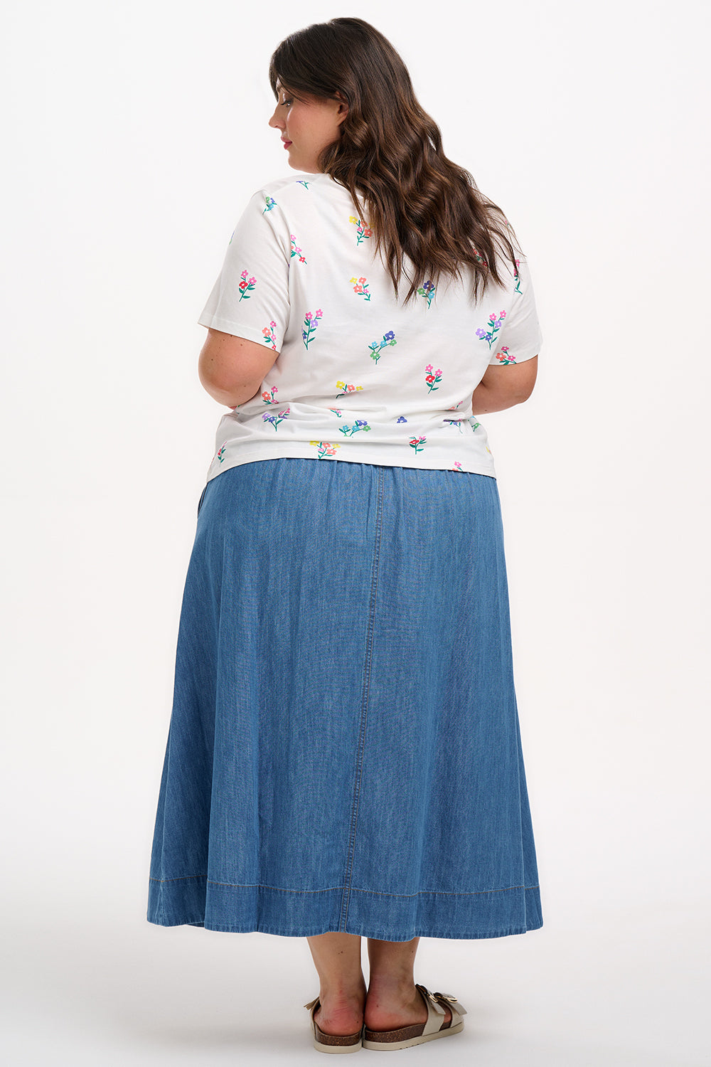 A woman smiling and wearing an off-white t-shirt with a pattern of small, colorful floral sprigs.