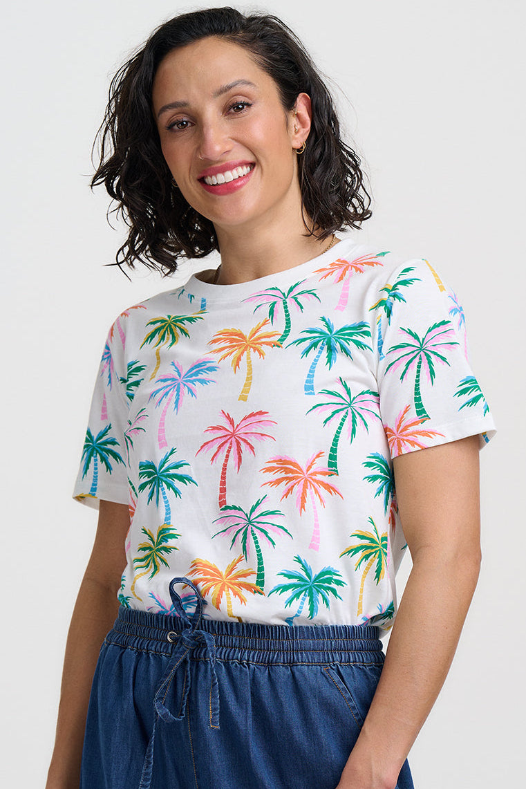 Woman wearing a colorful palm tree pattern shirt and blue shorts on a white background