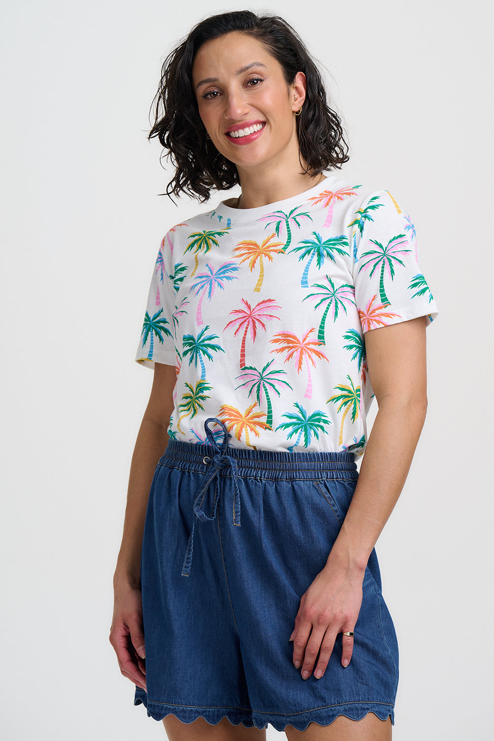 Woman wearing a colorful palm tree pattern shirt and blue shorts on a white background