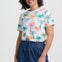 Woman wearing a colorful palm tree pattern shirt and blue shorts on a white background