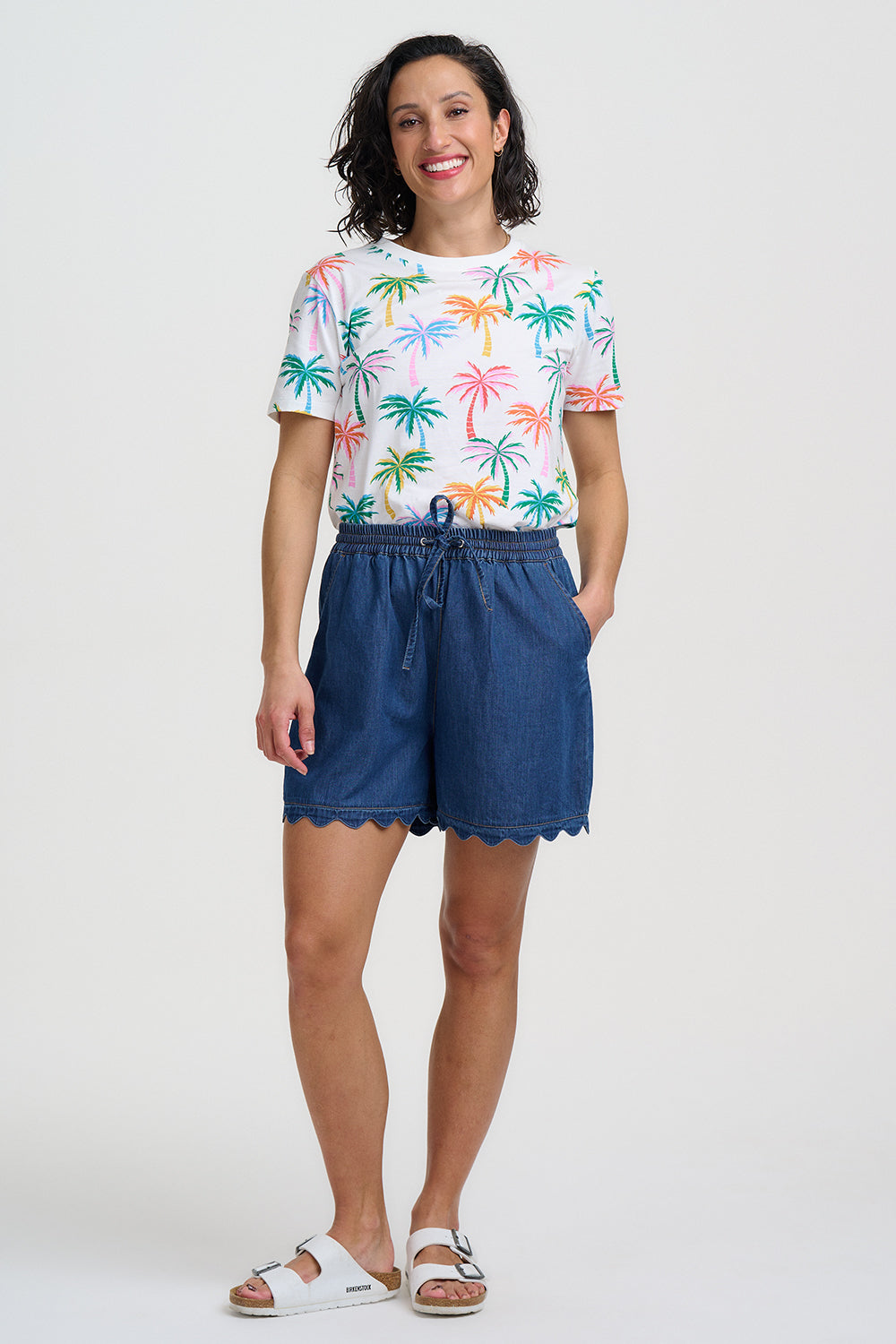 Woman wearing a colorful palm tree t-shirt and blue shorts on a white background