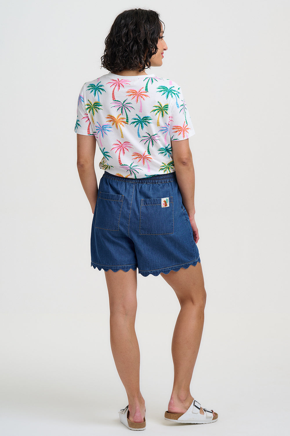 Person wearing a colorful palm tree shirt and blue shorts on a white background