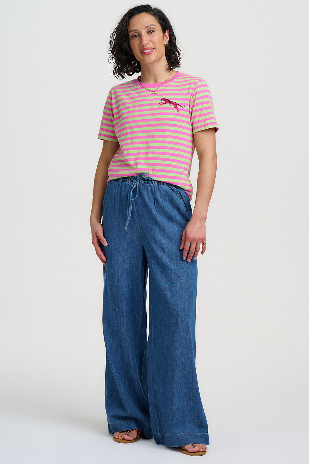 Woman wearing a pink and white striped shirt and blue wide-leg pants on a white background
