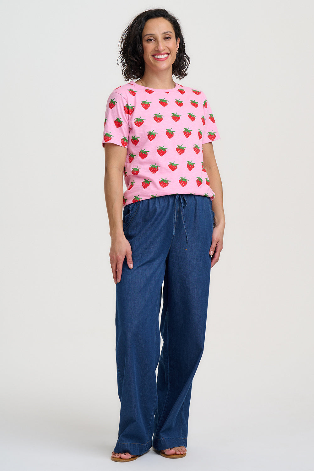 Woman wearing a pink t-shirt with strawberry pattern and blue pants on a white background