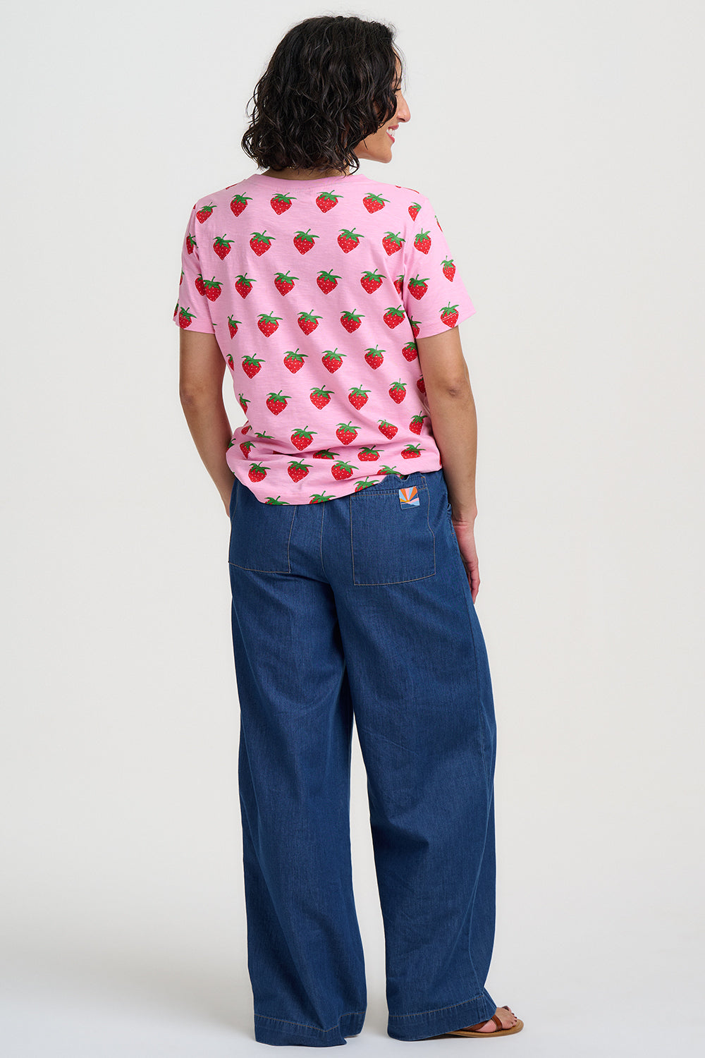 Person wearing a pink strawberry-patterned shirt and blue jeans on a white background