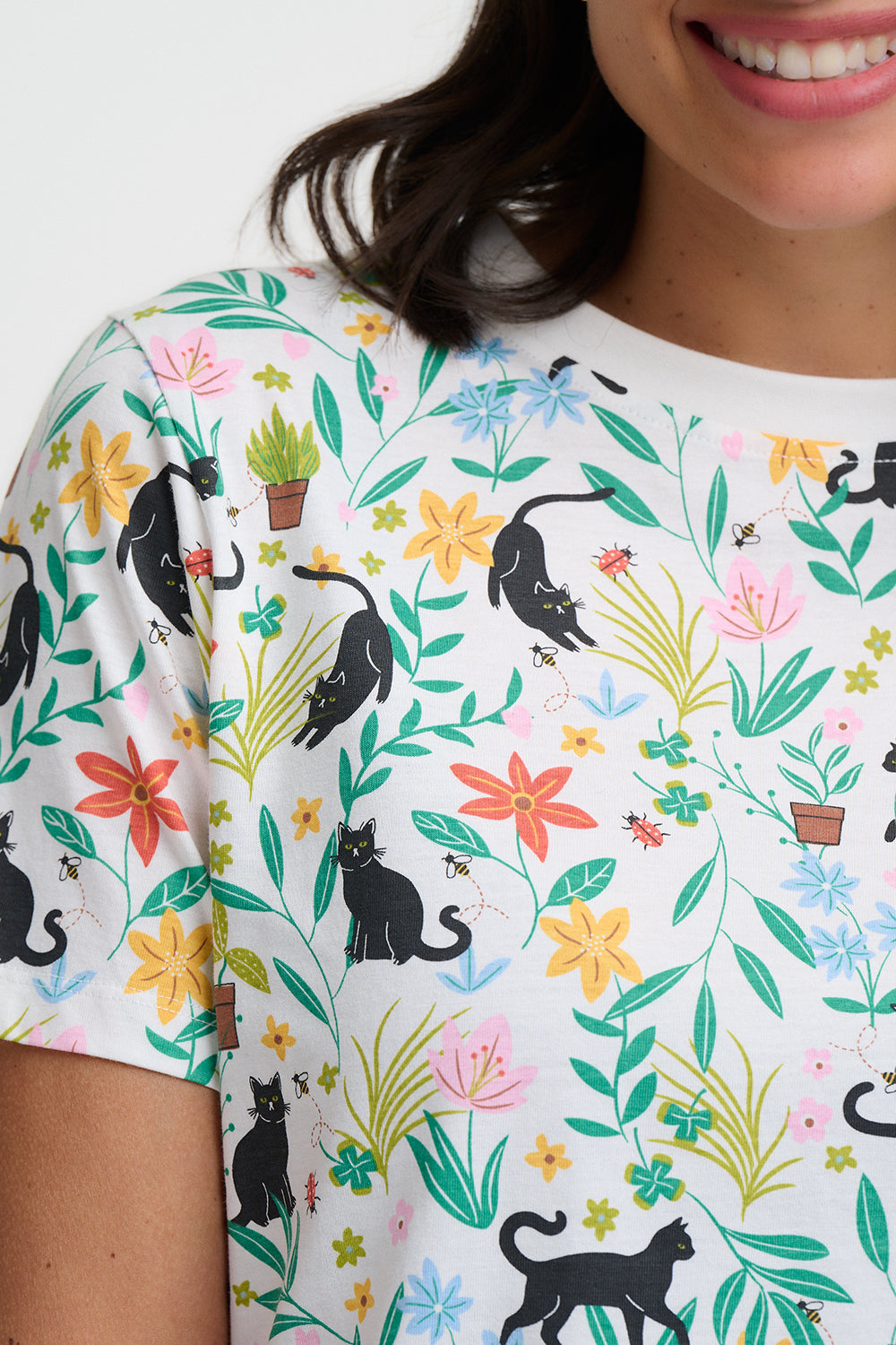 Person wearing a t-shirt with a colorful pattern of black cats, flowers, and plants.