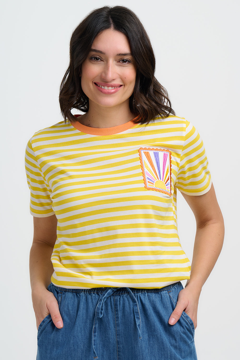 Woman wearing a yellow and white striped t-shirt with a colorful pocket design on a plain background
