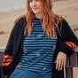 Woman with red hair wearing a black cardigan, blue striped shirt, and jeans outdoors.