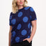 Woman wearing a navy blue top with large blue polka dots on a white background