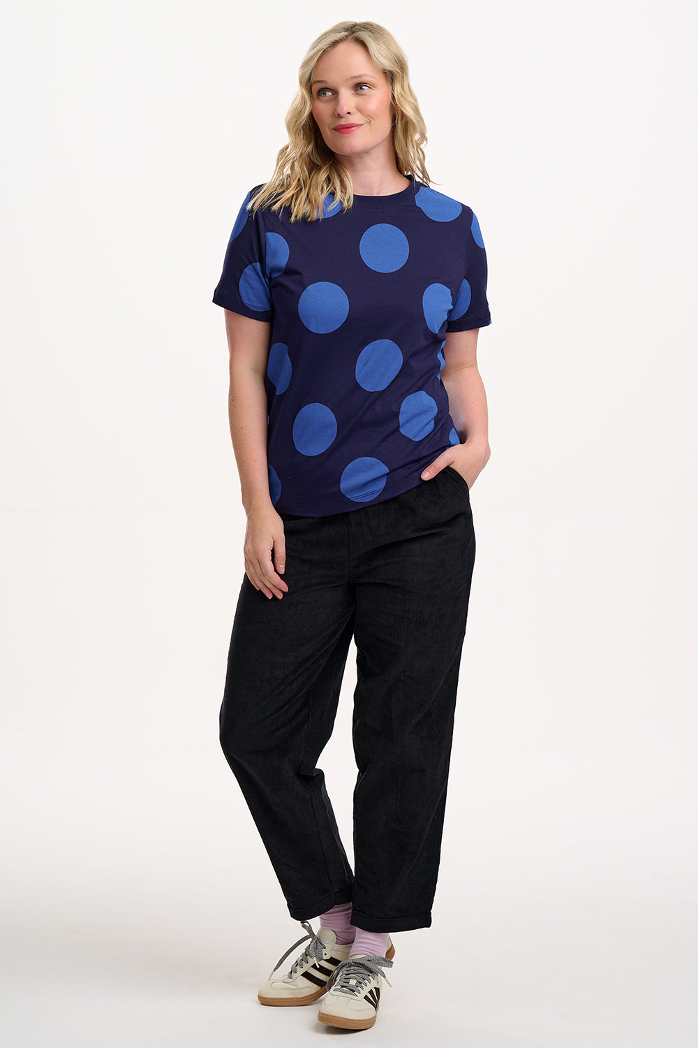 Woman wearing a navy blue t-shirt with large blue polka dots and black pants on a white background