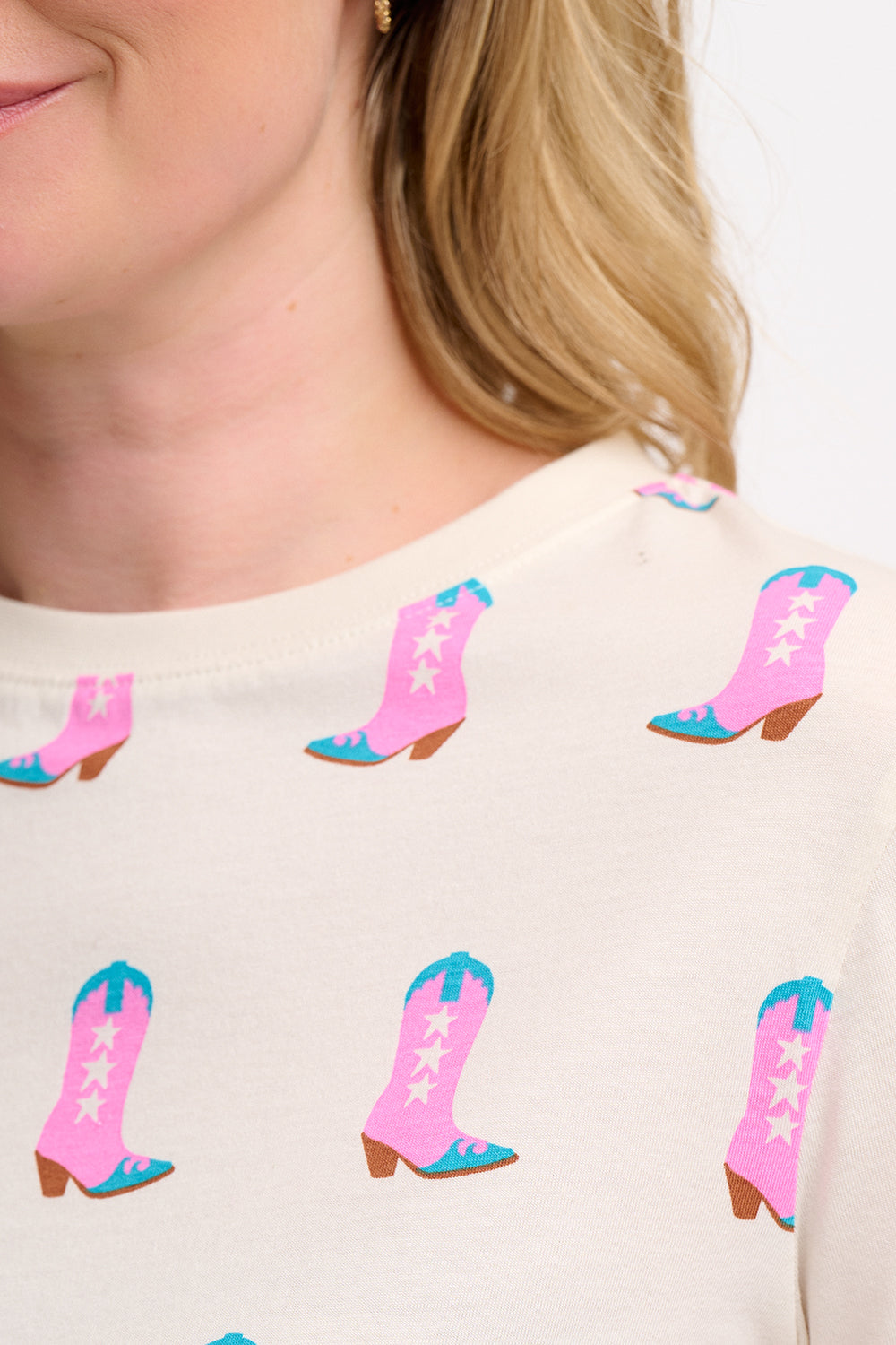 A woman smiling and wearing an off-white t-shirt with a pattern of cowgirl boots in pink and blue