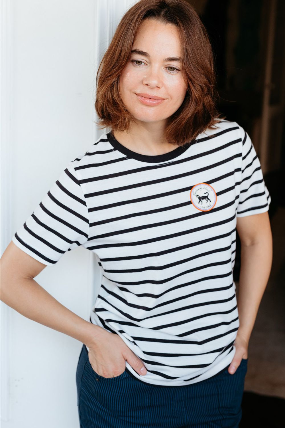 Woman wearing a black and white striped t-shirt with a small logo, standing against a plain background.