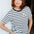 Woman wearing a black and white striped t-shirt with a small logo, standing against a plain background.